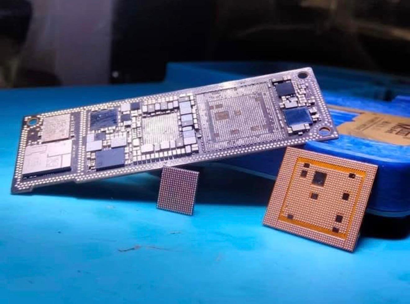 A reballed iPhone logic board on a blue repair mat at E11EVEN MOBILE, with the CPU and NAND chips lifted off beside it